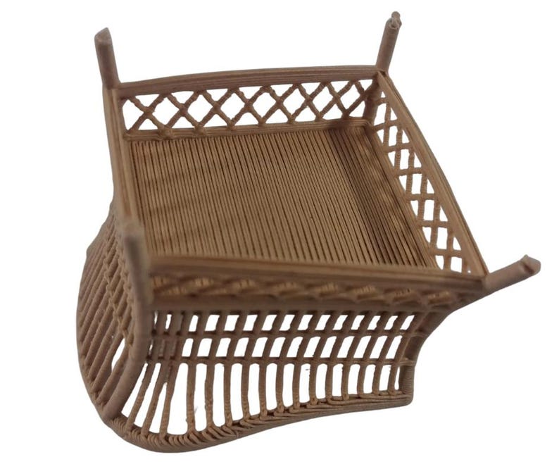 May include: A light brown, 3D-printed miniature square basket or container featuring a textured, ribbed base and a decorative lattice-style fence around the top perimeter, supported by four small, vertical corner posts extending upwards.