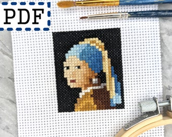 May include: Cross-stitch pattern of Johannes Vermeer's "Girl with a Pearl Earring" with blue and yellow accents. The image is on white fabric with a black background. The word "PDF" is in the upper left corner. Two paintbrushes are above the cross-stitch.