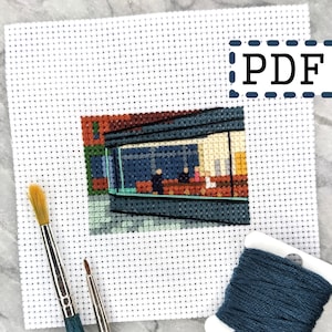 Pode incluir: Um padrão de ponto cruz de uma pintura abstrata colorida com uma vista de uma sala através de uma janela, onde as pessoas estão sentadas em cadeiras. O padrão está em uma tela Aida branca com um novelo de fio de bordar azul e duas escovas.