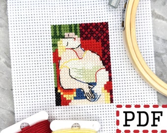 May include: Cross stitch pattern of a colorful abstract portrait with a person in a white shirt. The pattern is on white Aida cloth with red and yellow embroidery floss.