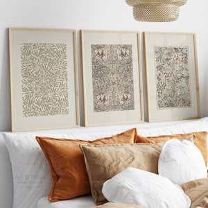 Puede incluir: Tres impresiones enmarcadas con patrones botánicos en tonos marrones, verdes y blancos. Las impresiones están colgadas en una pared blanca sobre una cama con almohadas marrones y blancas.