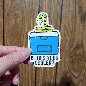 May include: A white sticker with a blue cooler and a green snake on top. The text "Is this your cooler?" is below the cooler.