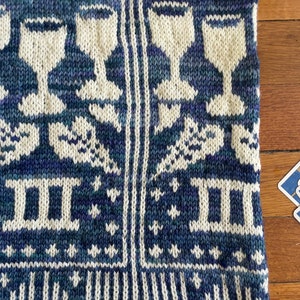 Pu&ograve; includere: Un tessuto di maglia blu e bianco con un motivo di stelle, bicchieri di vino e il numero romano II. Il tessuto ha un bordo bianco.