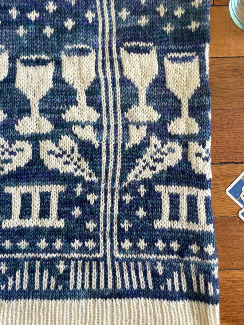 Pu&ograve; includere: Un tessuto di maglia blu e bianco con un motivo di stelle, bicchieri di vino e il numero romano II. Il tessuto ha un bordo bianco.