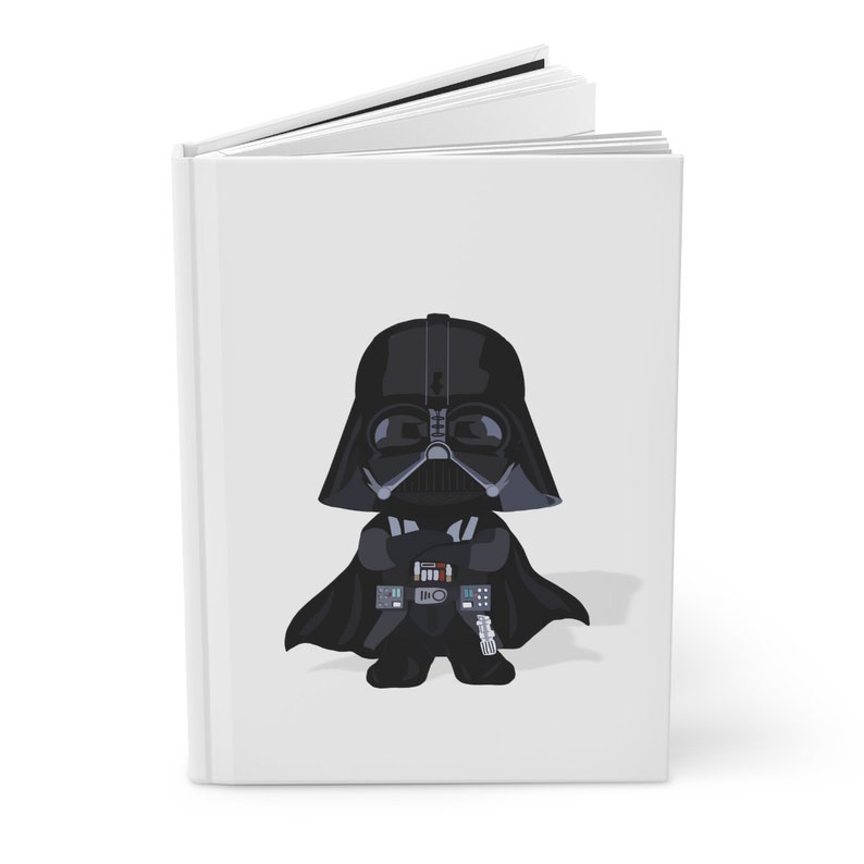Op de afbeelding: Wit hardcover notitieboek met een cartoon illustratie van Darth Vader. Het personage is afgebeeld in zwart met een gedetailleerde helm en cape. Het notitieboek is open en toont blanco witte pagina's.