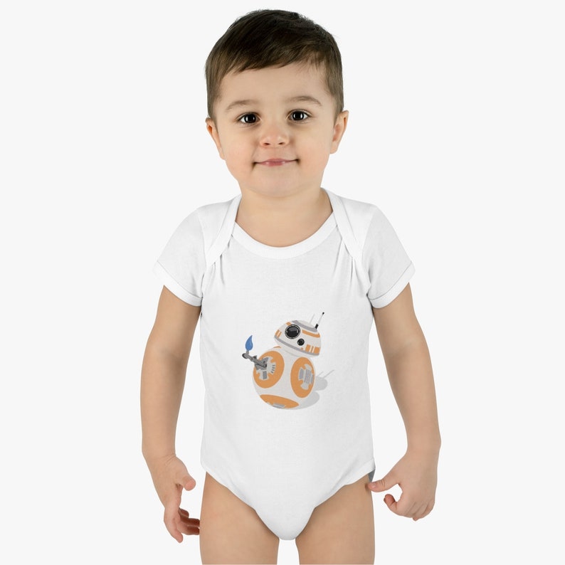 Op de afbeelding: Witte babybody met een afbeelding van het Star Wars-personage BB-8. Het BB-8-ontwerp is oranje, wit en grijs. De body heeft korte mouwen en een drukknoopsluiting.