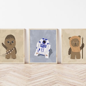 Op de afbeelding: Drie ingelijste prints met Star Wars-personages. Chewbacca, R2-D2 en een Ewok zijn afgebeeld in cartoonstijl. De print van Chewbacca heeft een beige achtergrond, R2-D2 heeft een blauwe achtergrond en de Ewok heeft een beige achtergrond. De frames zijn lichtbruin.