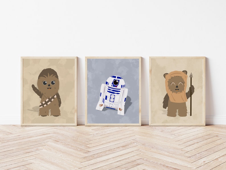Op de afbeelding: Drie ingelijste prints met Star Wars-personages. Chewbacca, R2-D2 en een Ewok zijn afgebeeld in cartoonstijl. De print van Chewbacca heeft een beige achtergrond, R2-D2 heeft een blauwe achtergrond en de Ewok heeft een beige achtergrond. De frames zijn lichtbruin.