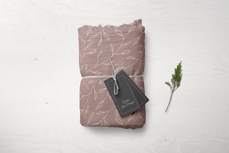 Puede incluir: Un paquete de tela rosa con un patr&oacute;n floral blanco est&aacute; atado con una cuerda blanca y dos etiquetas negras. Las etiquetas tienen texto blanco que dice "Crafted Love Designs".