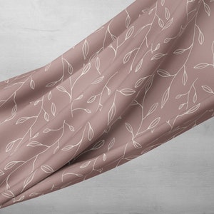 Puede incluir: Una tela suave de color rosa con un patr&oacute;n floral blanco. La tela est&aacute; drapeada sobre una superficie gris claro.