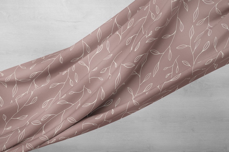 Puede incluir: Una tela suave de color rosa con un patr&oacute;n floral blanco. La tela est&aacute; drapeada sobre una superficie gris claro.