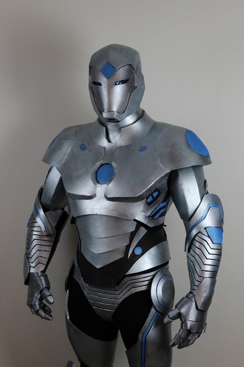 May include: A silver and blue superhero costume. The costume features a helmet, chest armor, and arm and leg coverings. Blue accents are visible on the shoulders, arms, and chest. The suit is made of a metallic material.