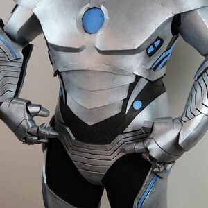 May include: Silver and blue futuristic armor costume. The costume features a metallic silver finish with blue accents on the shoulders, chest, and arms. The design includes layered plates and a central blue circular element on the chest.