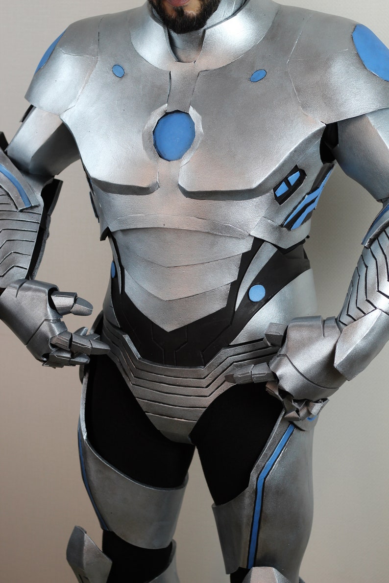 May include: Silver and blue futuristic armor costume. The costume features a metallic silver finish with blue accents on the shoulders, chest, and arms. The design includes layered plates and a central blue circular element on the chest.