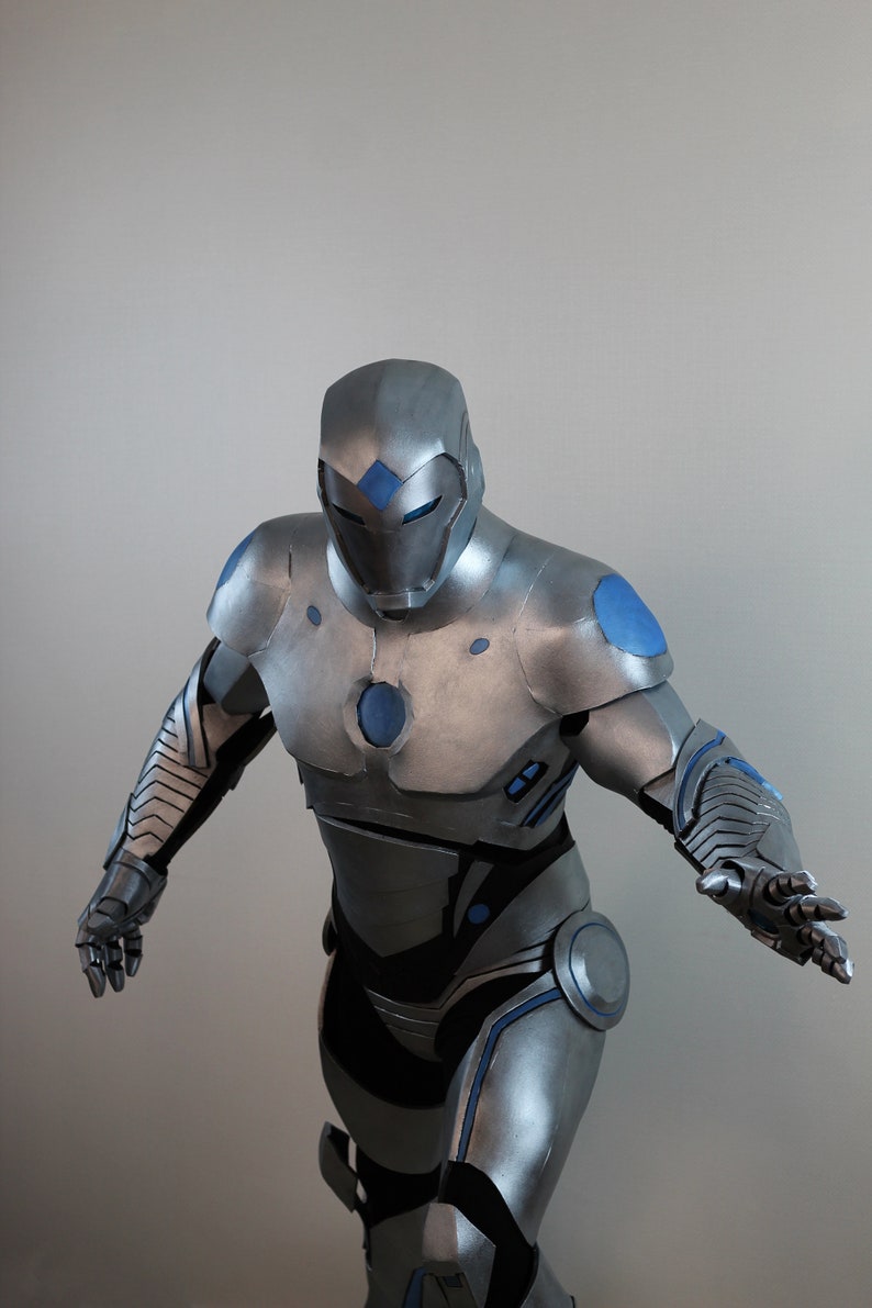 May include: A silver and blue superhero costume. The suit features a helmet with a diamond-shaped blue accent, blue circles on the shoulders, and blue accents on the arms and legs. The costume is metallic and detailed.