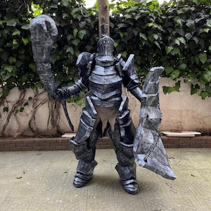 Puede incluir: Un disfraz completo de caballero medieval con armadura gris oscuro. El disfraz incluye un casco, una placa para el pecho y una armadura para las piernas. El caballero sostiene un gran garrote en una mano y un escudo en la otra.