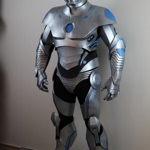 May include: A full-body silver and blue superhero costume. The suit has a helmet, chest plate, shoulder pads, arm and leg armor, and gloves. Blue accents are on the shoulders, chest, arms, and legs. The costume is made of a hard, metallic material.