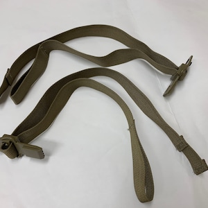 Op de afbeelding: Twee beige nylon banden met metalen gespen. De banden zijn ontworpen om te worden gebruikt als draaggreep of schouderband.