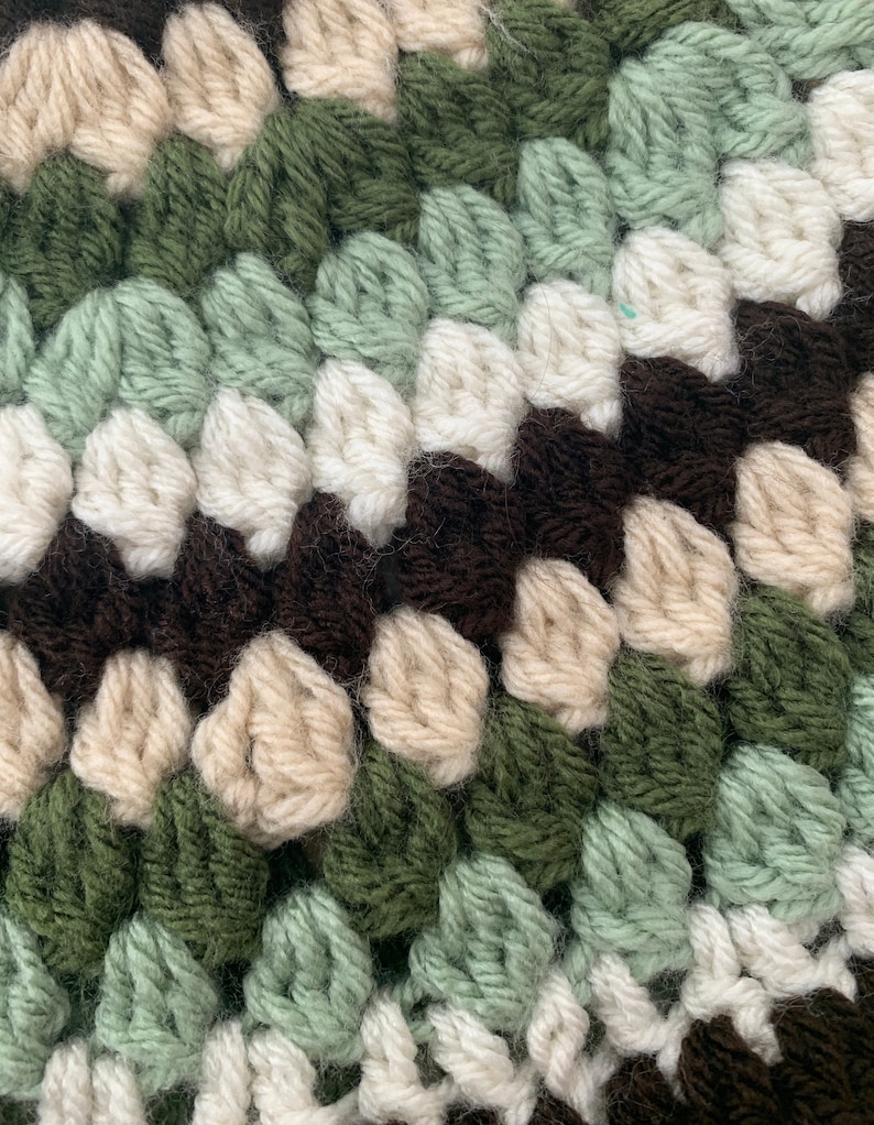 May include: Close-up of a crocheted fabric with a repeating pattern of brown, cream, green, and light green yarn.