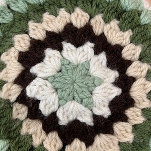 May include: Close-up of a crocheted round rug with a brown, white, and green color pattern. The center of the rug features a star-shaped design.