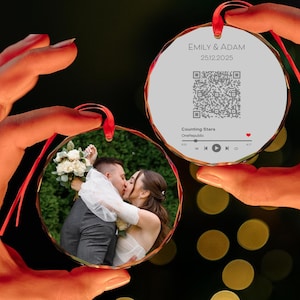 May include: Two round glass ornaments with red ribbon hangers. One ornament features a wedding photo of a couple kissing. The other ornament has the names "EMILY & ADAM 25.12.2025", a QR code, and music information for "Counting Stars" by OneRepublic.