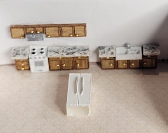 May include: Miniature kitchen set with a white refrigerator, stove, and sink. The cabinets are wooden with gold-colored knobs. The countertops have a marble-like pattern. The kitchen set is a dollhouse accessory.