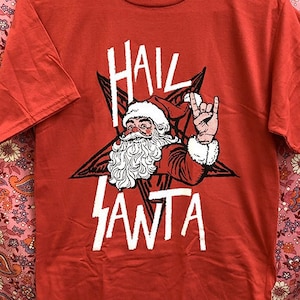 May include: Red t-shirt with a white graphic of Santa Claus with a pentagram behind him and the words "Hail Santa".