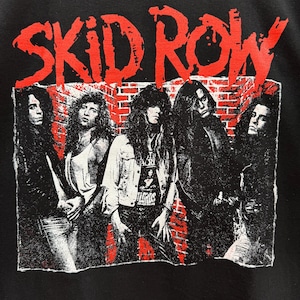 Puede incluir: Imagen en blanco y negro de una banda llamada "SKID ROW" con cinco miembros de pie frente a una pared de ladrillo. Los miembros de la banda visten ropa negra y tienen el pelo largo.