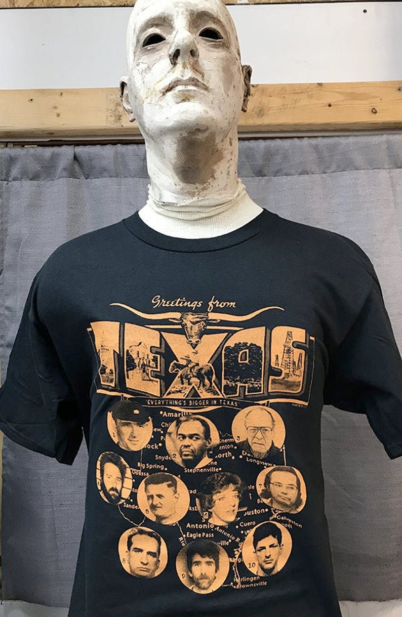 Puede incluir: Camiseta negra con un dise&ntilde;o de postal vintage que presenta un mapa de Texas con el texto "Greetings from Texas" y "Everything's Bigger in Texas". El dise&ntilde;o de la postal incluye un mapa de Texas con varias ciudades y pueblos, incluyendo Amarillo, Stephenville, San Antonio y Brownsville. La camiseta tambi&eacute;n presenta un dibujo de un toro longhorn.