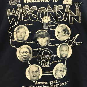 May include: A black t-shirt with a white graphic of a map of Wisconsin. The map is filled with photos of people and the text "Welcome to Wisconsin". The text "Awww, geez... People are just nicer here." is printed below the map.