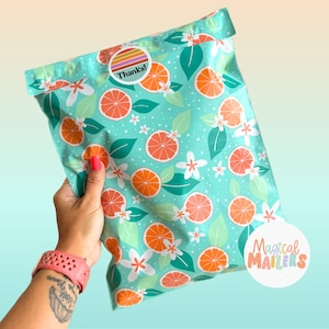 May include: A turquoise blue poly mailer with a repeating pattern of orange citrus fruit, white flowers, and green leaves. The mailer has a sticker that says "Thanks!" and a sticker that says "Magical Mailers".