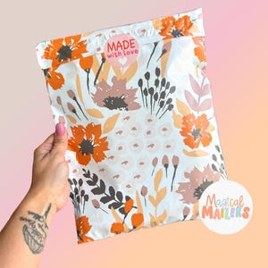 May include: A white floral patterned mailer bag with orange, peach, and brown flowers and leaves. The bag has a pink heart-shaped sticker that says "MADE with LOVE". The words "Magical Mailers" are printed on a white circle.