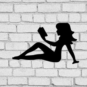 May include: A black silhouette of a person reclining and reading a book. The figure is positioned against a white brick wall. The person is seated with legs extended, holding the book up to read.