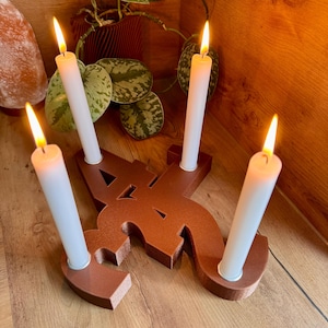 Op de afbeelding: Een bruine houten kandelaar in de vorm van de letter "A" met vier witte kaarsen die branden met gele vlammen. De kandelaar staat op een houten oppervlak.