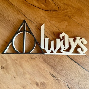 Könnte beinhalten: Schwarzes und weißes Holzschild mit dem Symbol der Heiligtümer des Todes und dem Wort "Always" in einer dekorativen Schrift.