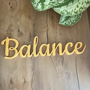 May include: A yellow wooden sign with the word "Balance" written in a cursive font.