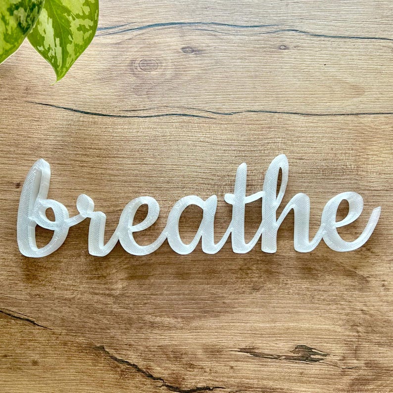 May include: White cursive word "breathe" on a wood background.