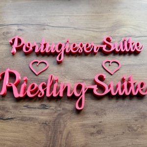May include: Two pink wooden signs with the words "Portugieser Suite" and "Riesling Suite" with a pink heart shape above each sign.