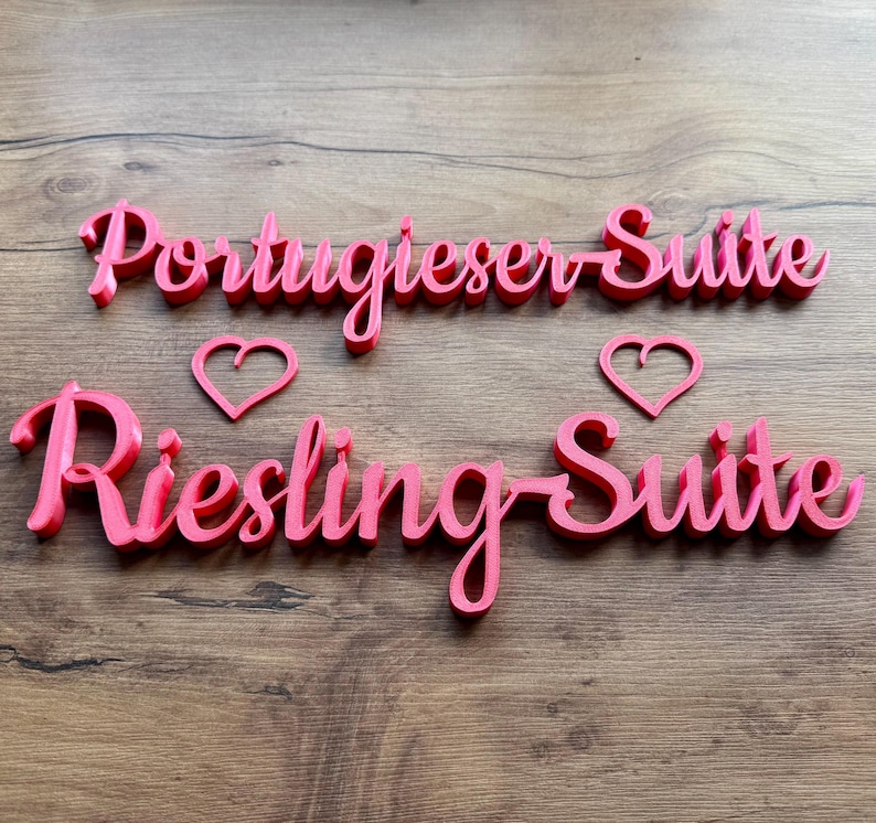 May include: Two pink wooden signs with the words "Portugieser Suite" and "Riesling Suite" with a pink heart shape above each sign.