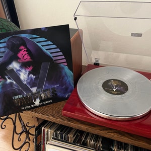 Könnte beinhalten: Ein Vinyl-Schallplattenalbum mit einem Cover, das eine stilisierte Abbildung einer Figur in einem Kapuzenmantel mit dem Text "THERE'S NO SUCH THING AS VAMPIRES" zeigt. Die Schallplatte liegt auf einem roten Plattenspieler.