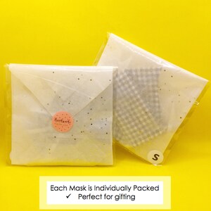 Puede incluir: Dos sobres de papel de seda blanco con puntos de purpurina dorada, uno con una pegatina rosa "Handmade with Love" y el otro con una tela de cuadros blancos y grises en el interior. El texto "Each Mask is Individually Packed" y una marca de verificaci&oacute;n con el texto "Perfect for gifting" est&aacute;n impresos sobre un fondo amarillo.