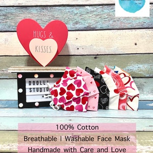 Puede incluir: Un conjunto de cinco mascarillas faciales con tem&aacute;tica de San Valent&iacute;n hechas de 100% algod&oacute;n. Las mascarillas presentan diferentes patrones de corazones y remolinos en rosa, rojo, blanco y negro. Las mascarillas est&aacute;n hechas a mano con cuidado y amor y est&aacute;n hechas en los Estados Unidos. El texto "HUGS & KISSES" es visible en la imagen.