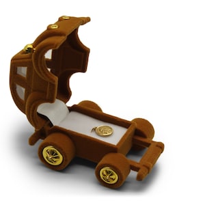 May include: A brown velvet ring box shaped like a vintage car with a gold-colored trim. The box is open and a small gold-colored pendant is inside.