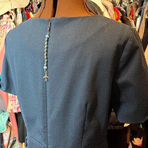 May include: A dark blue dress with short sleeves and a small airplane charm hanging from the back neckline.