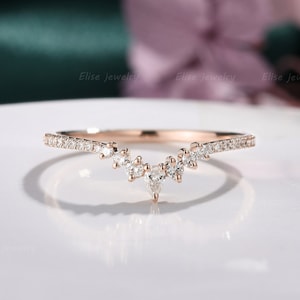Op de afbeelding: Een delicate ring van roségoud met een V-vormige band van kleine diamanten en een grotere peervormige diamant in het midden.