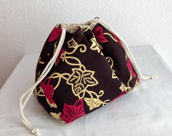 Pode incluir: Uma bolsa de cordão marrom com um padrão floral em tons de rosa, amarelo e branco. A bolsa tem um cordão branco e é feita de tecido.