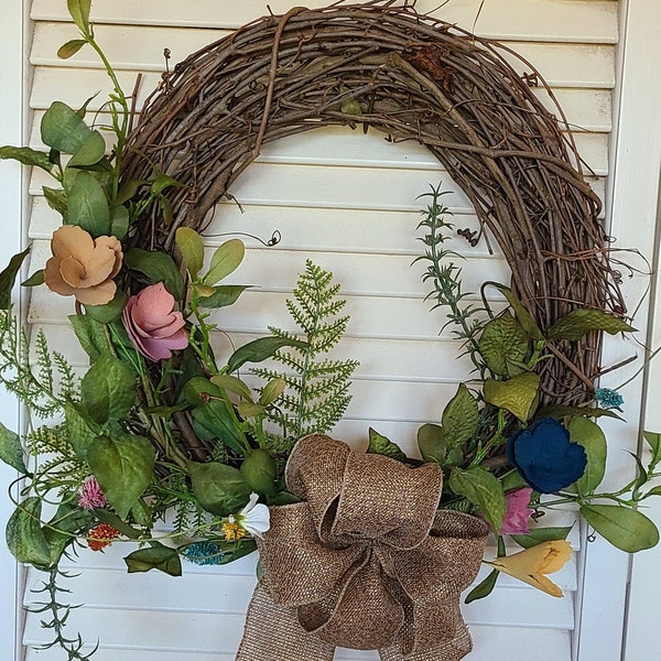 Grapevine wreath. Spring/Summer freeform lite and airy with chipwood flowers, butterflies. Bow is burlap look with gold threads.