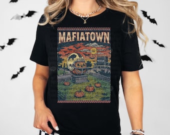 May include: Black t-shirt with a vintage-style graphic featuring the text "MAFIATOWN". The graphic includes a pumpkin with a football helmet, pumpkins, and a graveyard scene. The shirt is a Halloween-themed design.