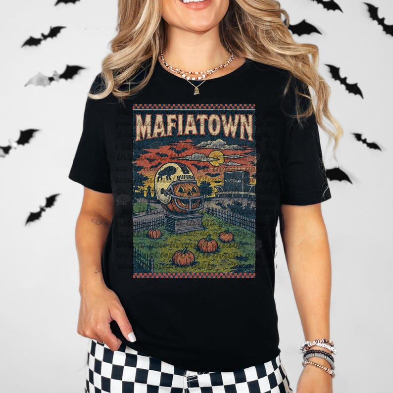 May include: Black t-shirt with a vintage-style graphic featuring the text "MAFIATOWN". The graphic includes a pumpkin with a football helmet, pumpkins, and a graveyard scene. The shirt is a Halloween-themed design.