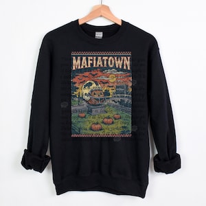May include: Black sweatshirt featuring a vintage-style graphic with the text "MAFIATOWN." The graphic includes a pumpkin carved like a football helmet, pumpkins, a fence, and a stadium under a sunset sky.